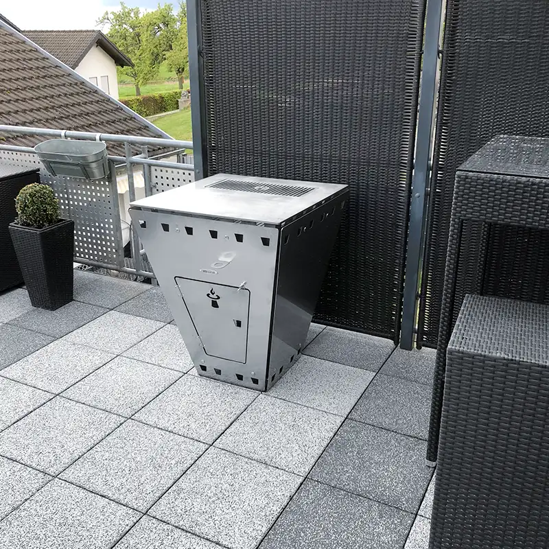 Eckige Feuerstelle Magnus aus Edelstahl steht auf einem Balkon neben schwarzen Sitzgelegenheiten