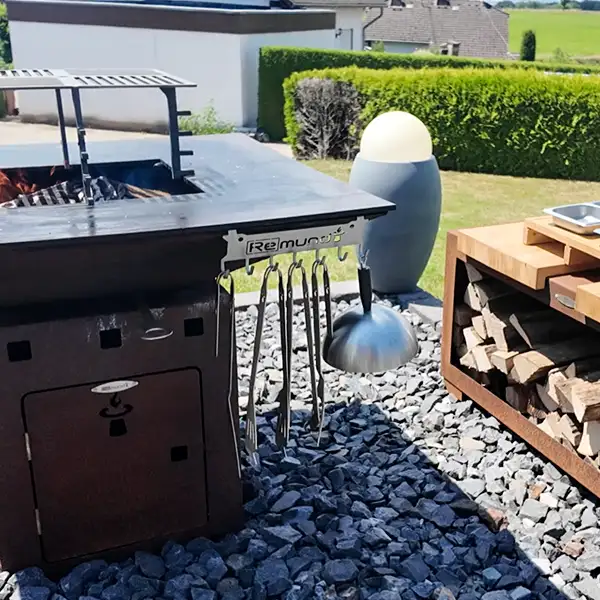 Remundi Cube Feuerstelle, die im Garten steht, daneben ein Holzlager