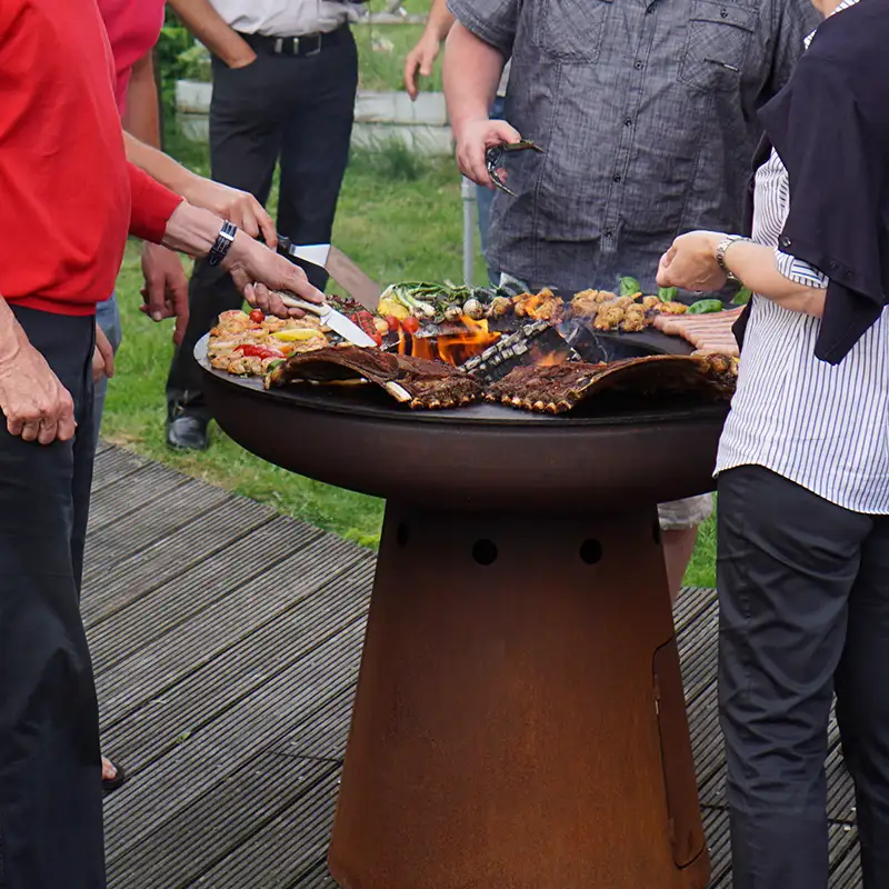 Mehrere Personen stehen vor der Remundi Nero Feuerstelle in einem Garten und braten Grillgut