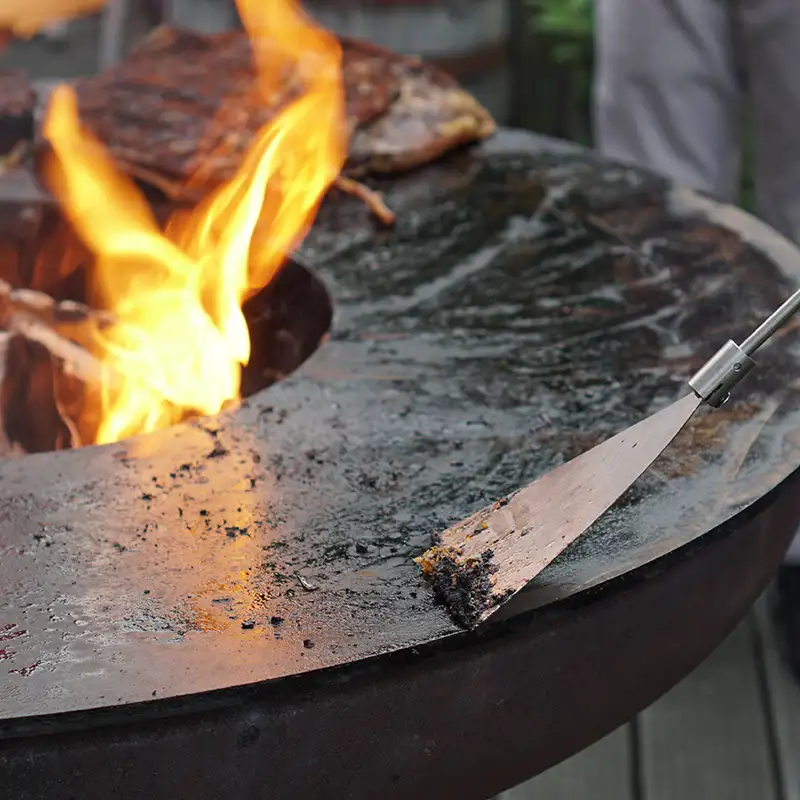 remundi-nero-l-reinigung Detailansicht wie jemand mit einem Edelstahl-Grillspatel die Grillplatte reinigt