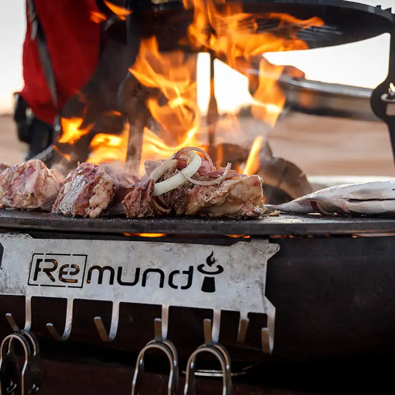 Detailansicht von Grillbesteckhalter aus Edelstahl an einer Remundi Feuerstelle, auf der Fleisch gegrillt wird