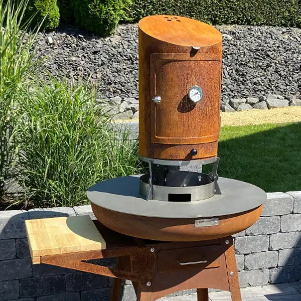 Der Smoker in Rostoptik mittig platziert über der Remundi Zelos Feuerstelle im Garten