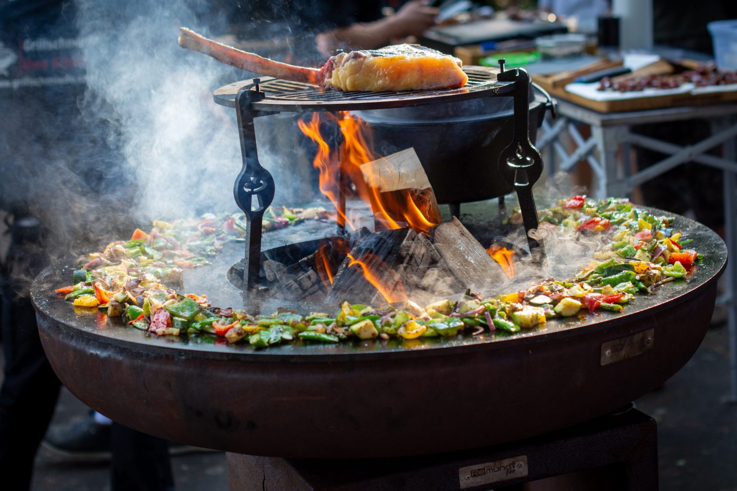 Seitenansicht der Remundi Feuerschale mit Grill: Zeigt die verschiedenen Temperaturzonen mit Fleisch im heißen Zentrum und Gemüse im kühleren Außenbereich.