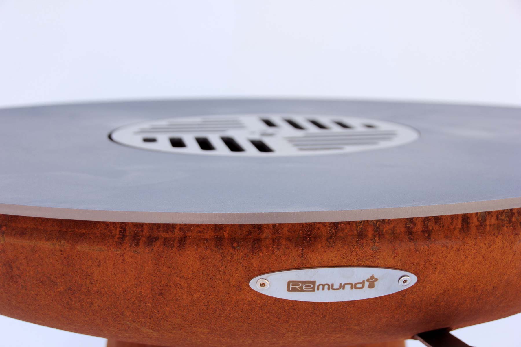 Nahaufnahme der Remundi Feuerplatte aus massivem Stahl mit dunkler Patina. Die Wölbung neigt sich zur Mitte, damit Fett ins Feuer läuft.