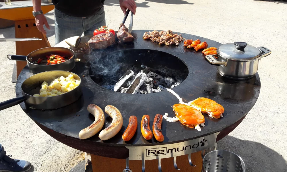 People_enjoying_the_moment_on_the_Remundi_fire_plate 3 people stand around the Remundi fire bowl with grill plate and enjoy the moment while barbecuing