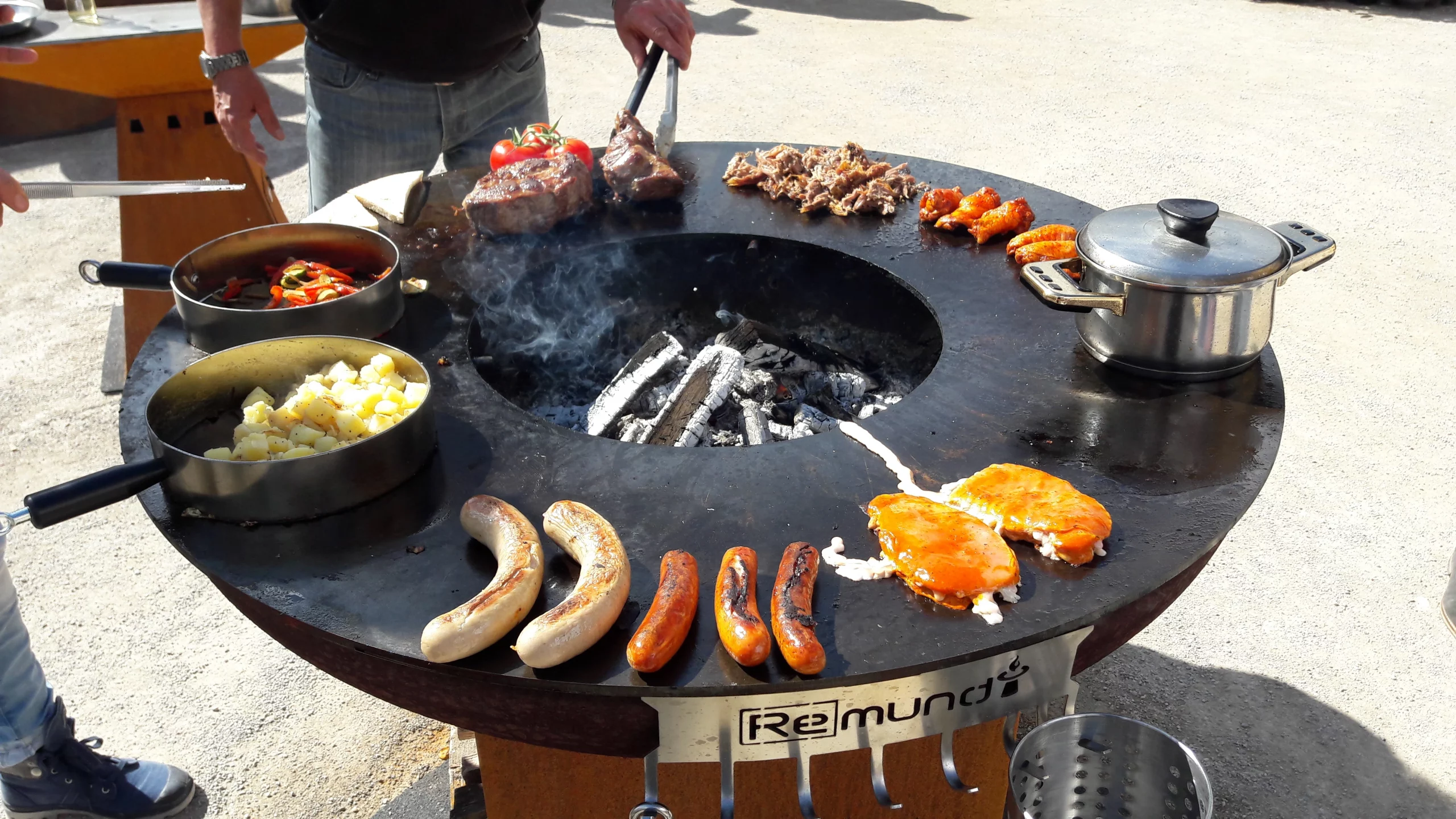 3 Menschen stehen um die Remundi Feuerschale mit Grillplatte und genießen den Moment beim Grillen
