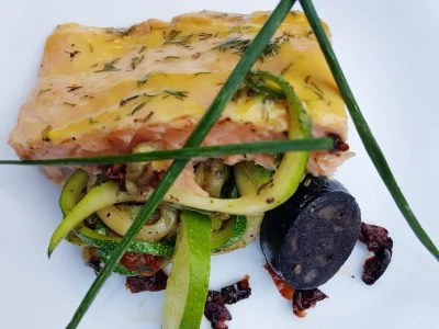 Lachsfilet auf Zedernholzplanke mit Blutwurst und Zucchinispaghetti auf der Remundi Feuerplatte angerichtet