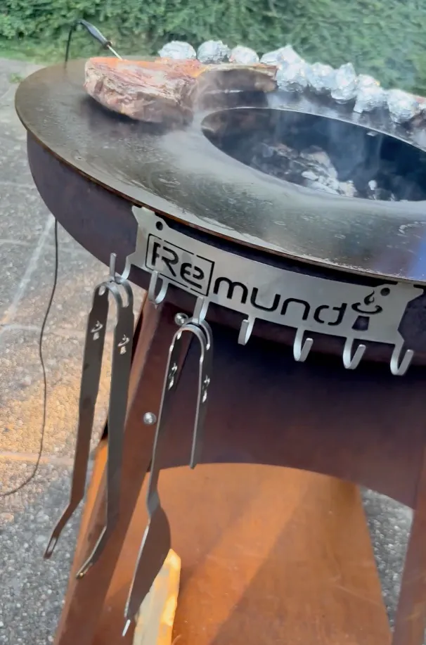 Grill cutlery holder mounted on the fire pit, with grill tongs and spatula hanging within reach